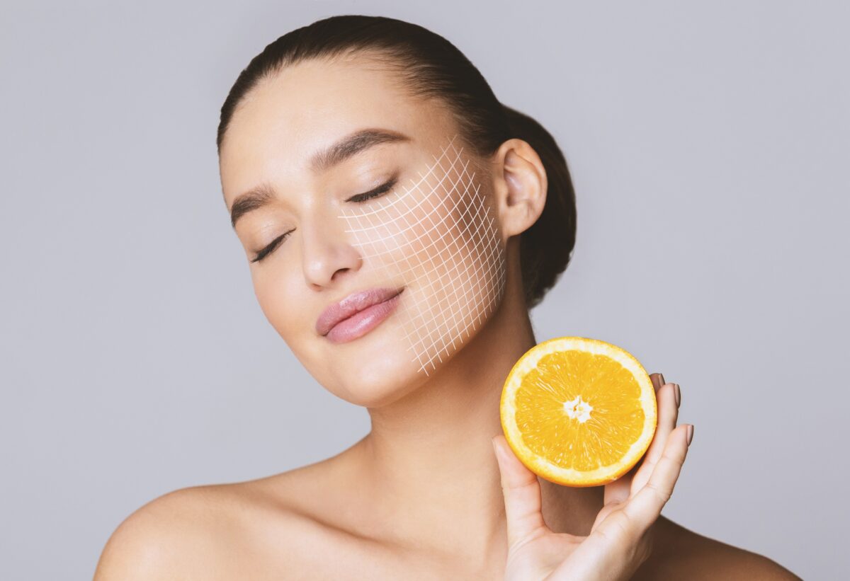 Vitamin C for skin. Delighted young pretty woman with closed eyes holding orange half over grey background