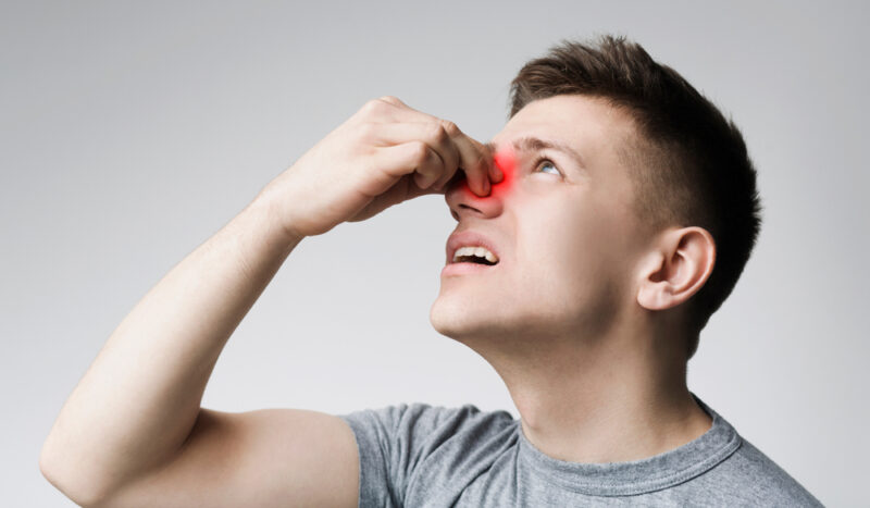 Epistaxis. Young man touching his bleeding nose, panorama, close up