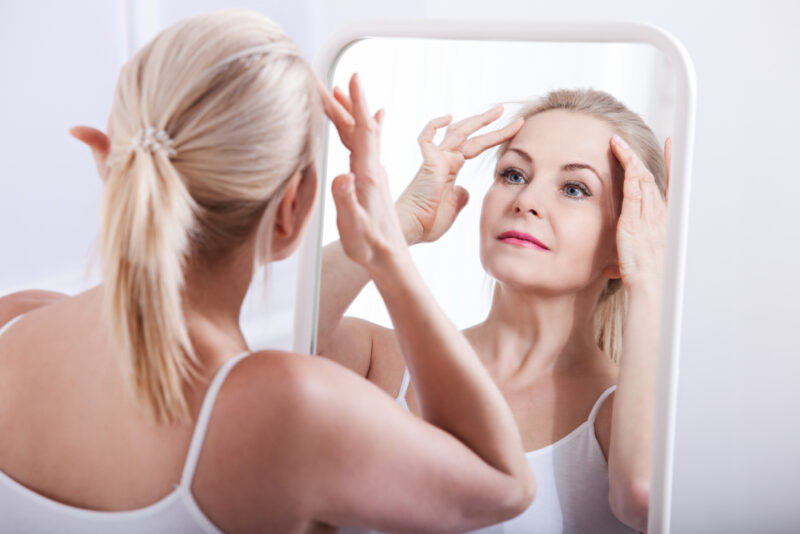 Middle aged woman looking at wrinkles in mirror. Plastic surgery and collagen injections