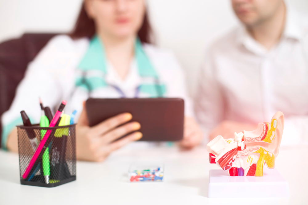 Female doctor otolaryngologist shows on the tablet information on the structure of the ear, throat and nose. Concept of ENT surgery, audiometry and tympanometry