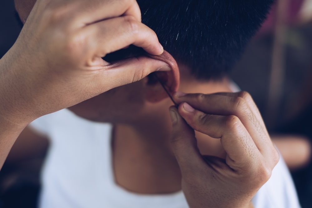 Closeup of hands manually cleaning a man's left ear of earwax using an ear pick. Selective focus.