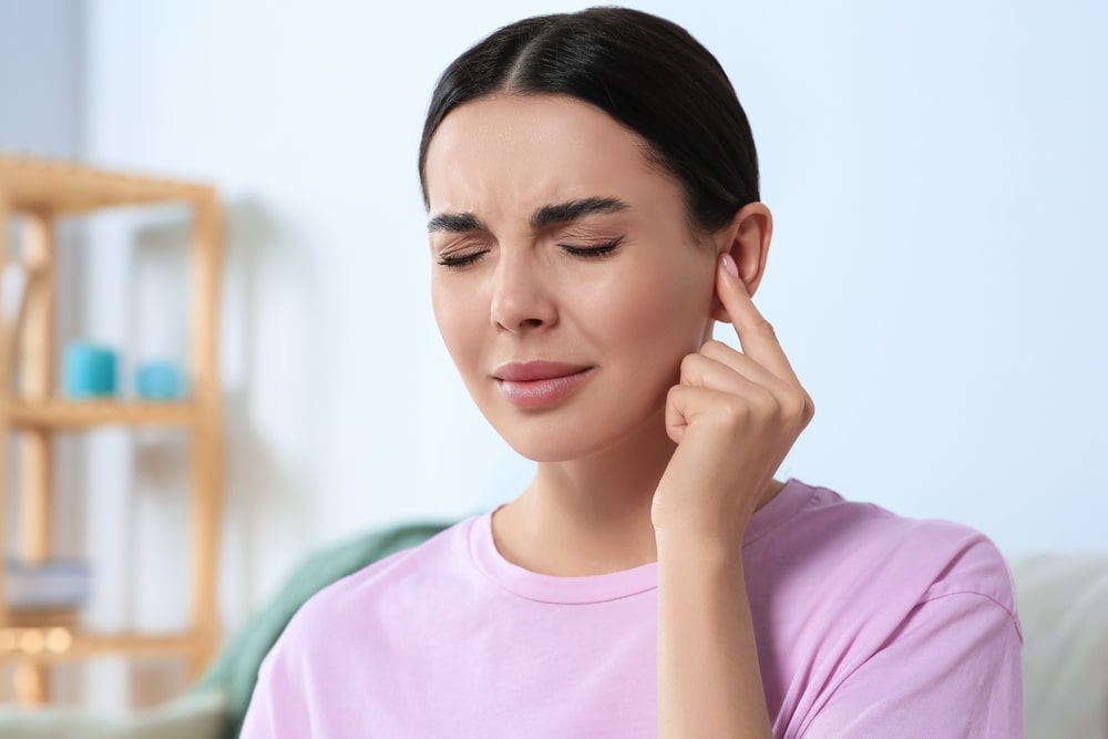 Young woman suffering from ear pain at home