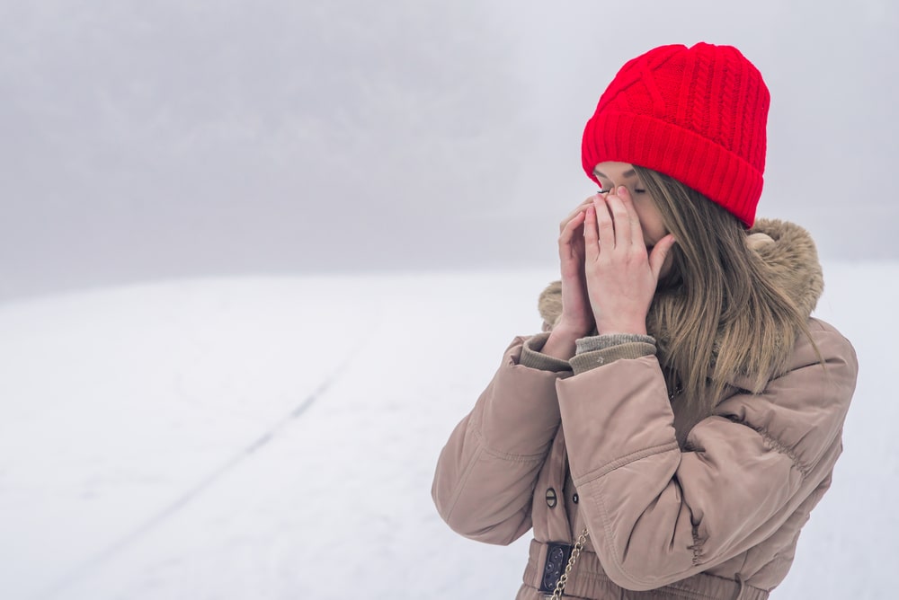 Young woman with sinus pressure pain. Portrait of suffering woman, light brown hair with red cup, pinching bridge of nose in pain and discomfort from sinus congestion, splitting headache.