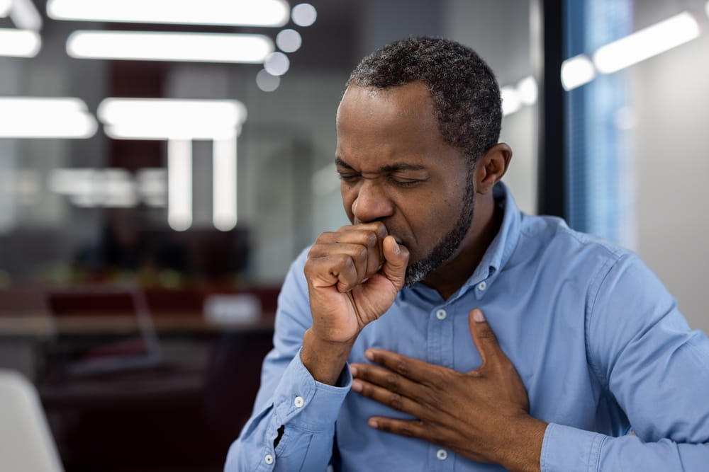 Concerned man coughing at work with hand on chest, indicating cold