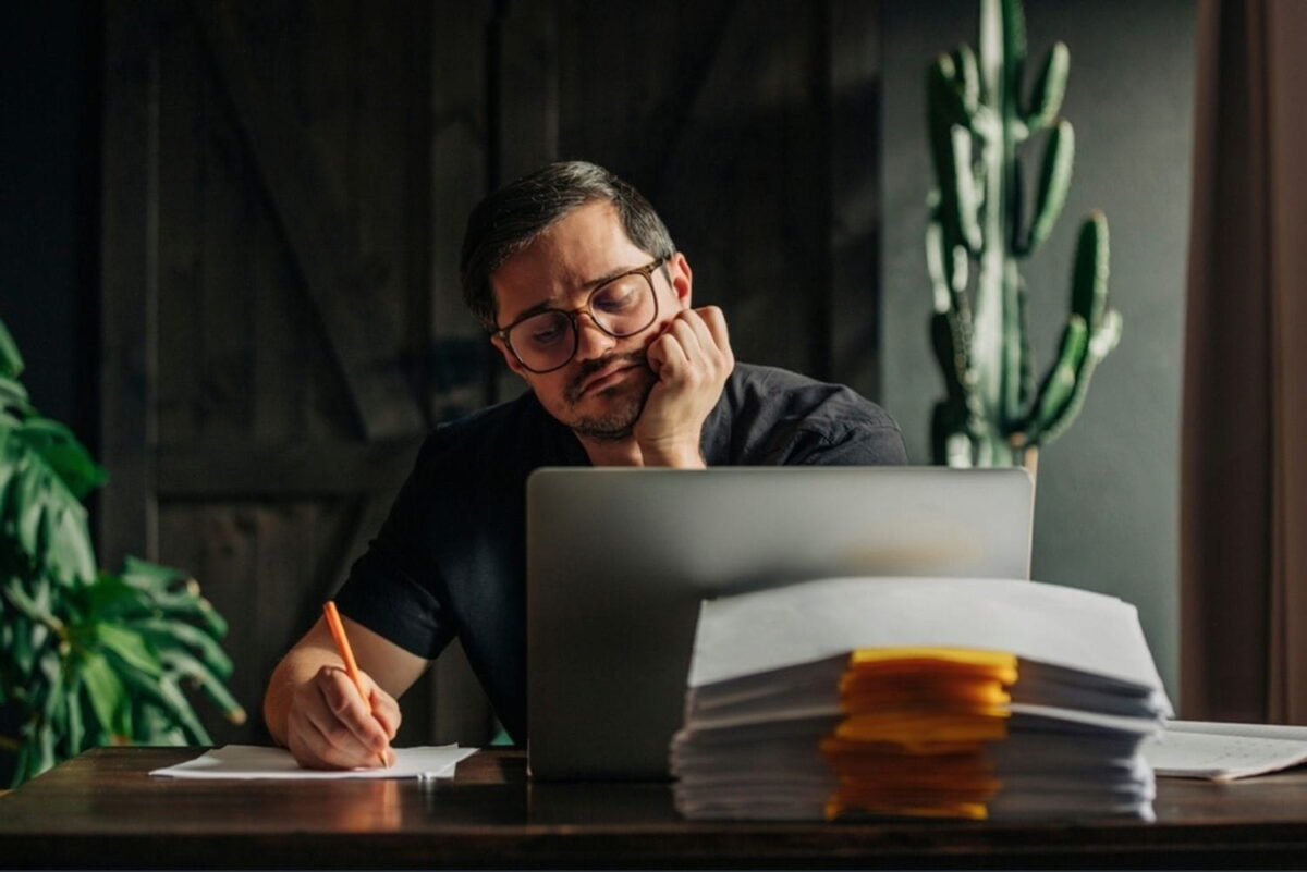 Man in dark shirt working remotely at home using laptop and writing