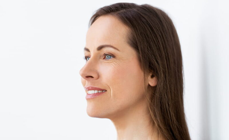 health and beauty concept - side view of happy smiling middle aged woman face