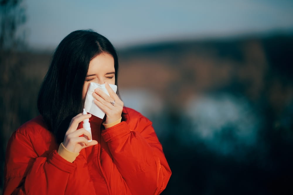 Woman Holding a Nasal Spray Blowing Her Nose feeling Cold. Sick girl suffering from winter allergies using a breathing relief medicine