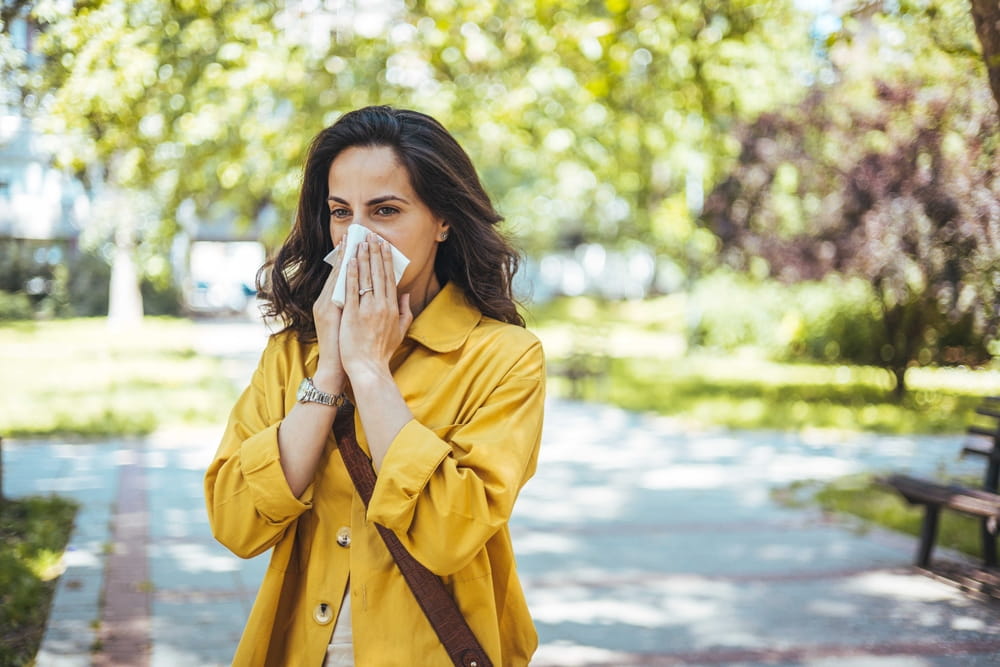 Shot of a young woman blowing her nose outside. Sneezing coughing ill young african woman using paper napkin, having runny nose