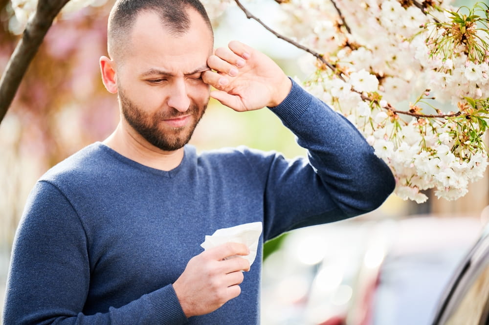 Man allergic suffering from seasonal allergy at spring in blossoming garden at springtime.