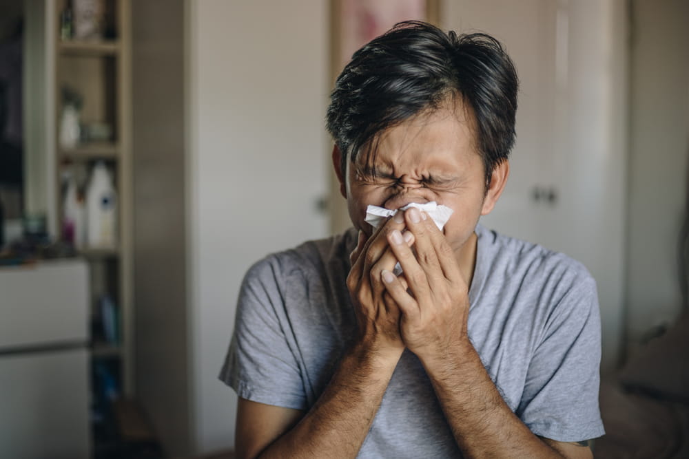 Young man with a cold blowing her runny nose with tissue. Asian man get sick sneezing from flu.
