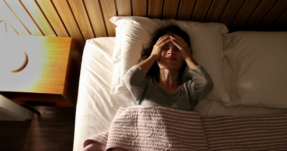 Worried woman unable to sleep suffering from insomnia. Person tossing and turning turning nightstand light ON