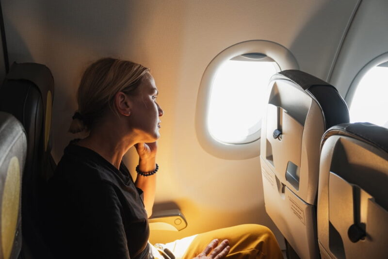 Passenger woman is flying in plane. Girl sitting in airplane looking out window going on trip vacation travel.