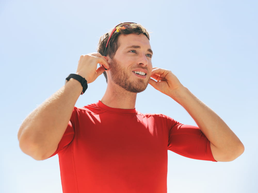 Young man putting on wireless headphone bluetooth connected to smartwatch earphones for fitness run outdoors