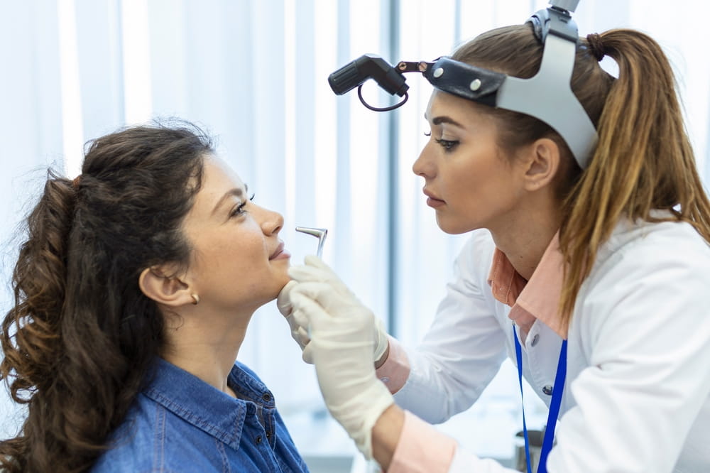 Doctor otorhinolaryngologist checking nose with otoscope of patient at hospital. Nasal congestion, sinusitis, allergy concept.