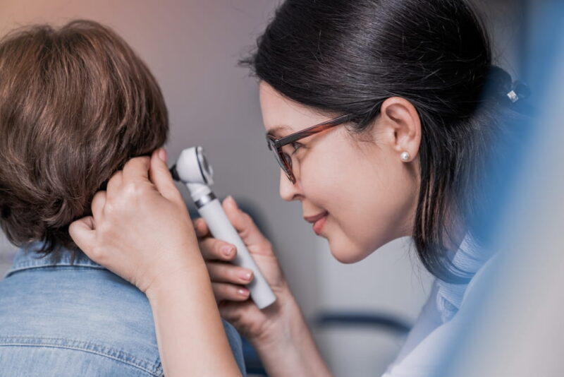 Close up of doctor examining boy's ear with otoscope in medical cabinet. Barotrauma laryngitis otitis ear treatment.