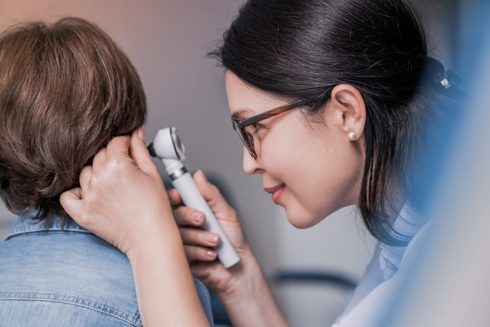 Close up of doctor examining boy's ear with otoscope in medical cabinet. Barotrauma laryngitis otitis ear treatment.
