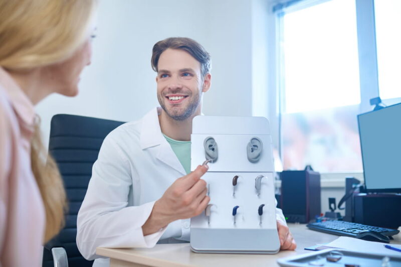 Friendly doctor offering different deaf aids to his a patient