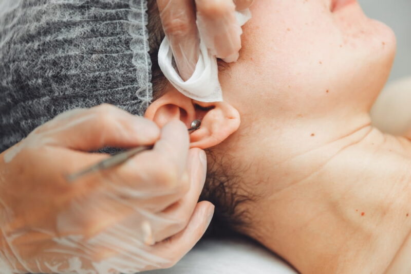 A young girl is lying on a couch during cosmetic procedures, over which a cosmetologist squeezes out fat deposits and pimples with a special metal tool.ear cleaning