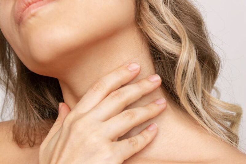 A cropped shot of a young blonde woman touching the neck with her hand