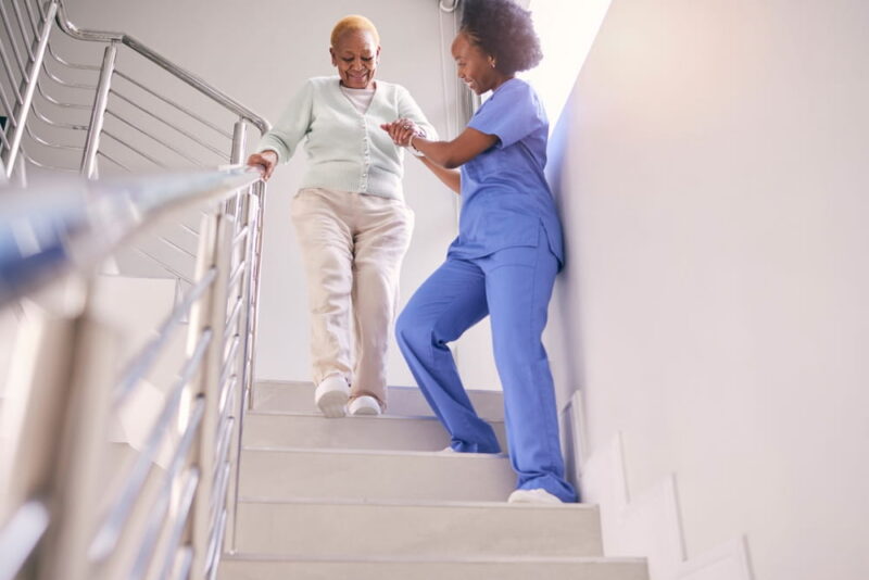 Steps, nurse and help elderly woman, holding hands and assistance in home.
