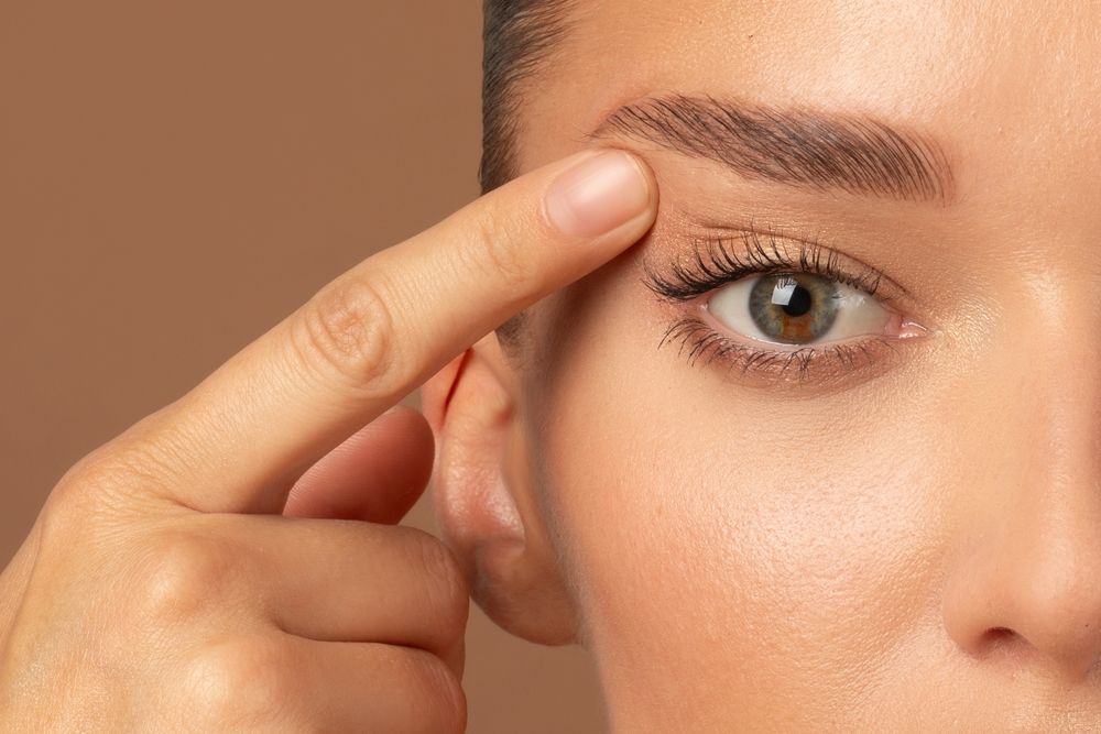 Closeup of young European woman pointing to the wrinkles on the upper eyelid, touching face.