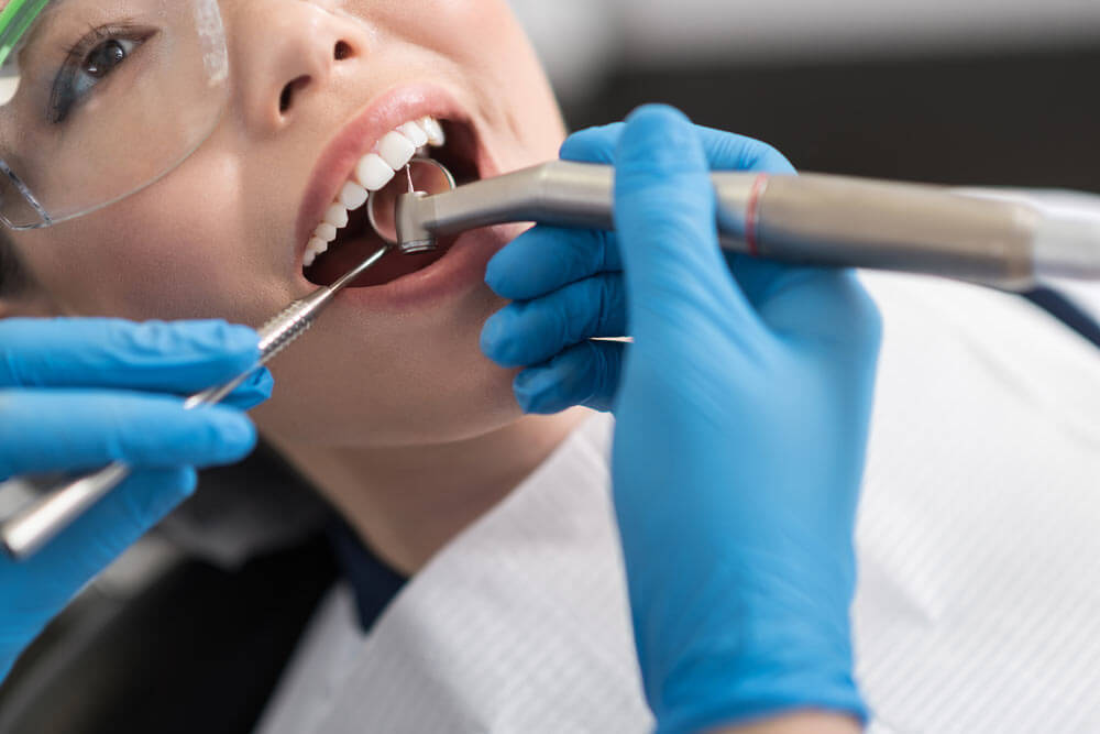 Dentist curing oral cavity of cheerful woman