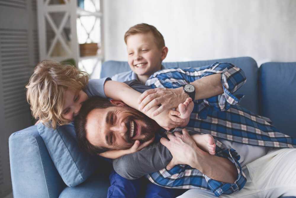 Smiling father and sons having fun on cozy couch