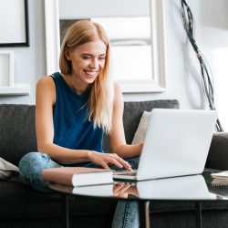 Happy young woman sitting on sofa using laptop