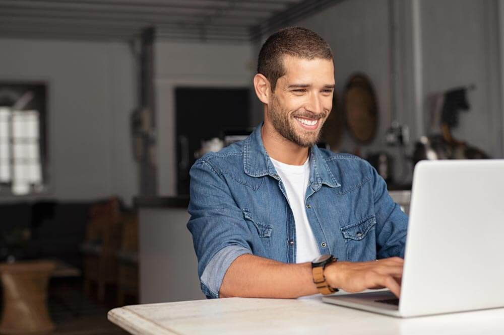 Happy young businessman using laptop at home