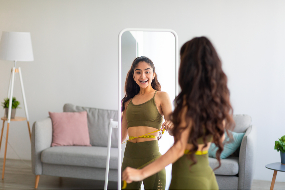 slim woman measuring her waist in front of mirror