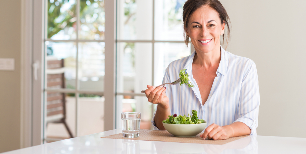 Middle aged woman eating fresh salad in a bowl at home
