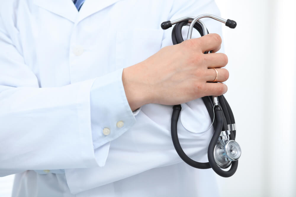 male doctor standing straight while holding stethoscope