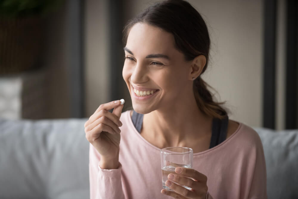 Smiling healthy young woman holding pill glass of water