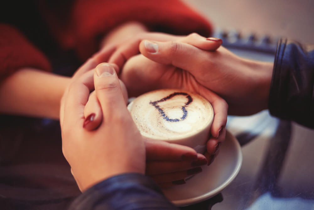 Four hands wrapped around a cup of coffee with heart