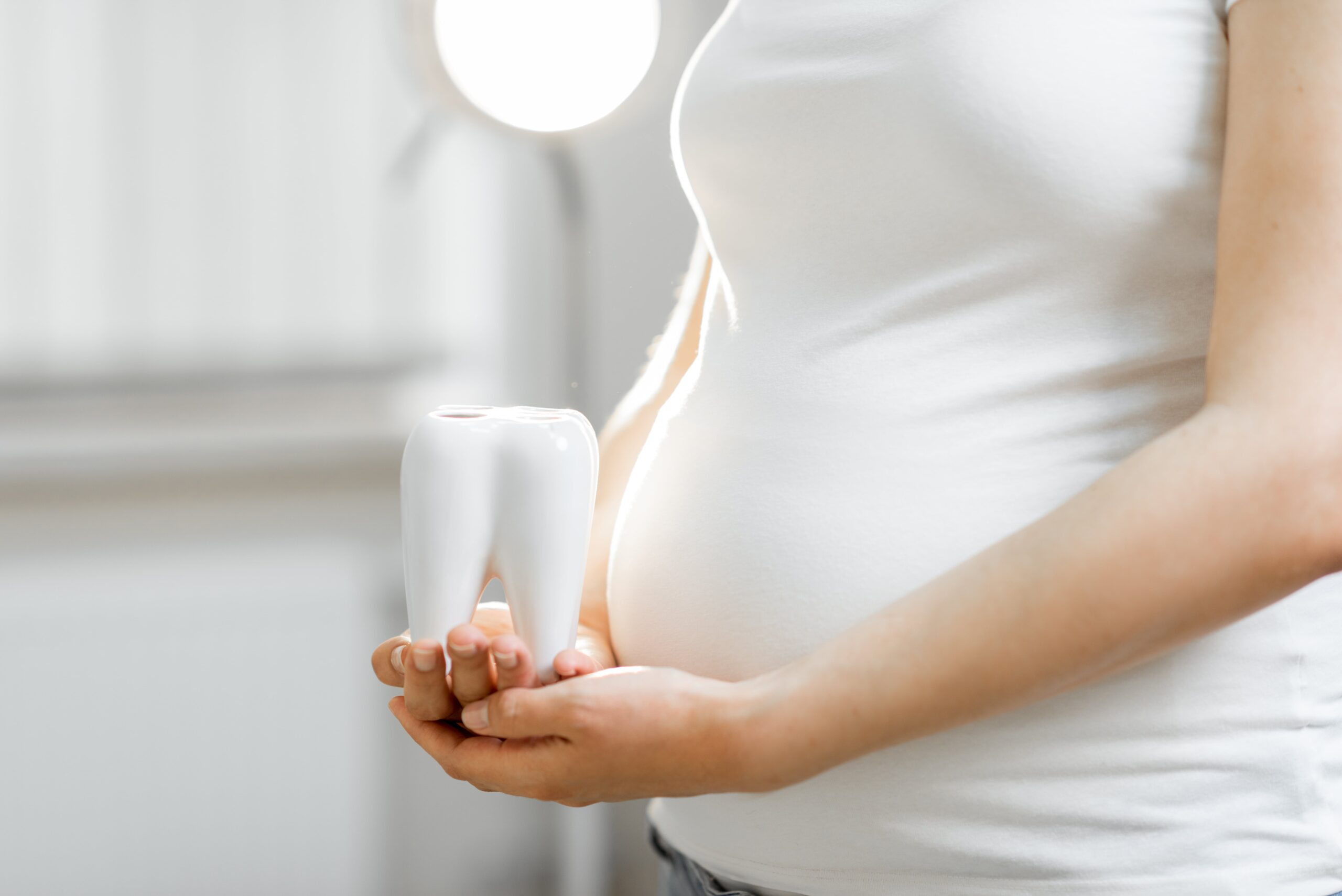 pregnant woman holding giant tooth beside her belly. concept for dental care during pregnancy