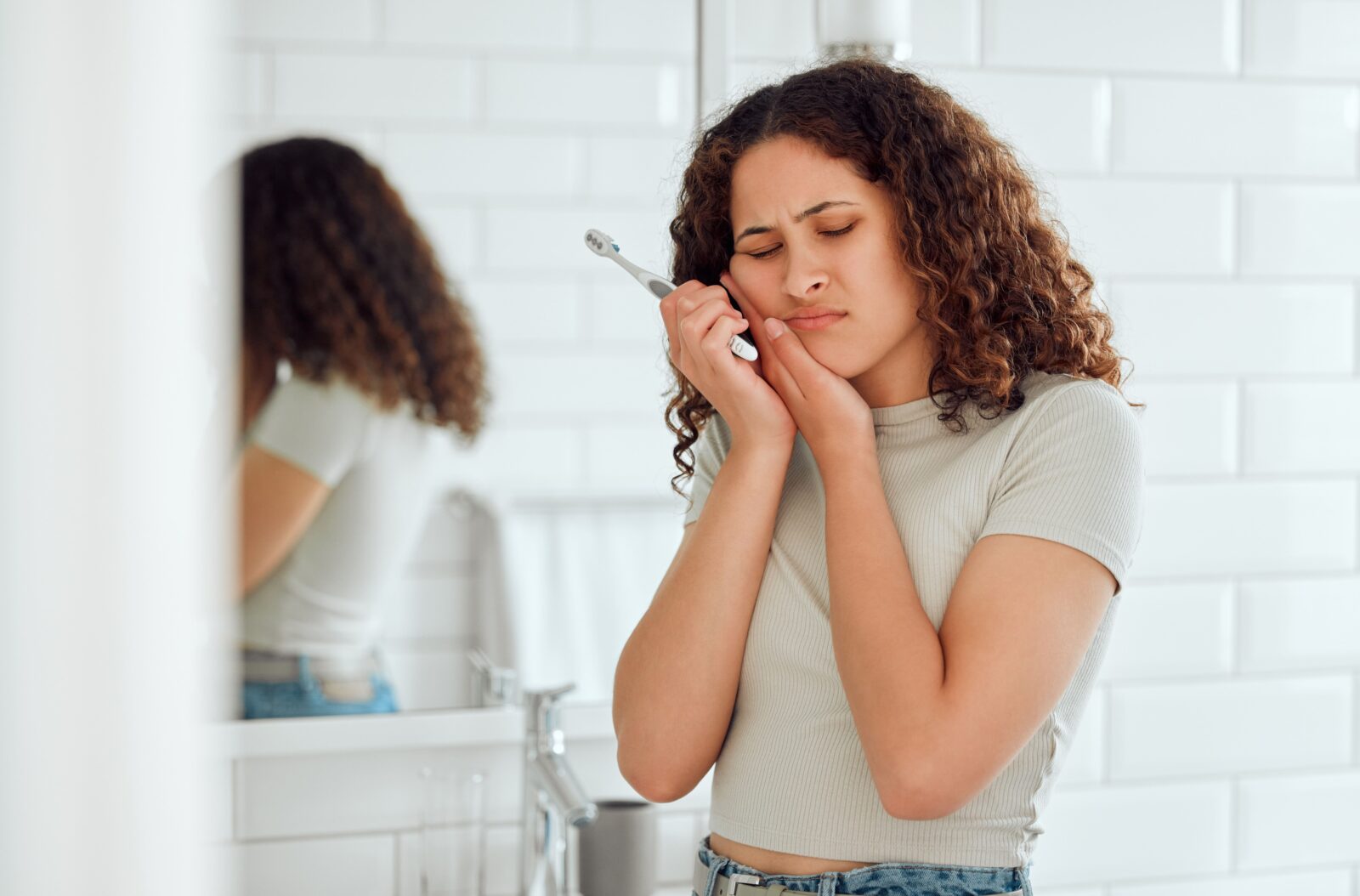 woman holding a toothbrush and her cheek in pain