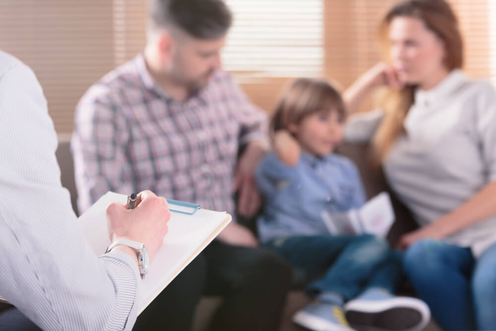 family psychotherapist writing notes in front of a couple with a child