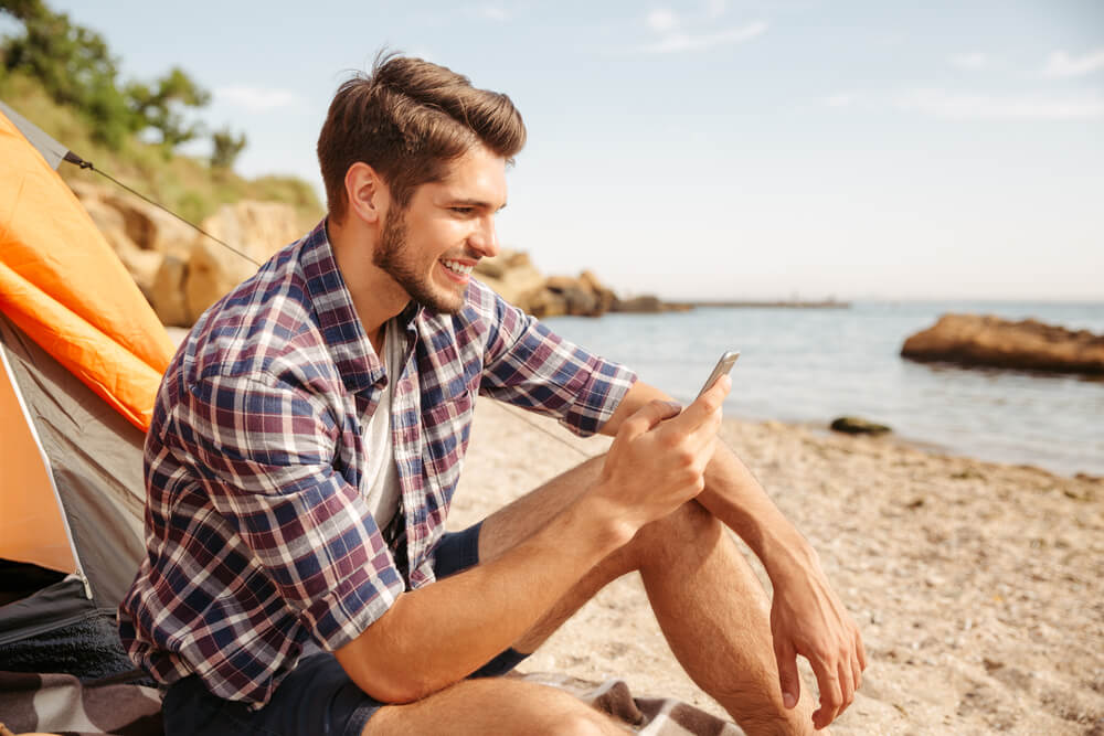 Smiling young man using smartphone at the beach