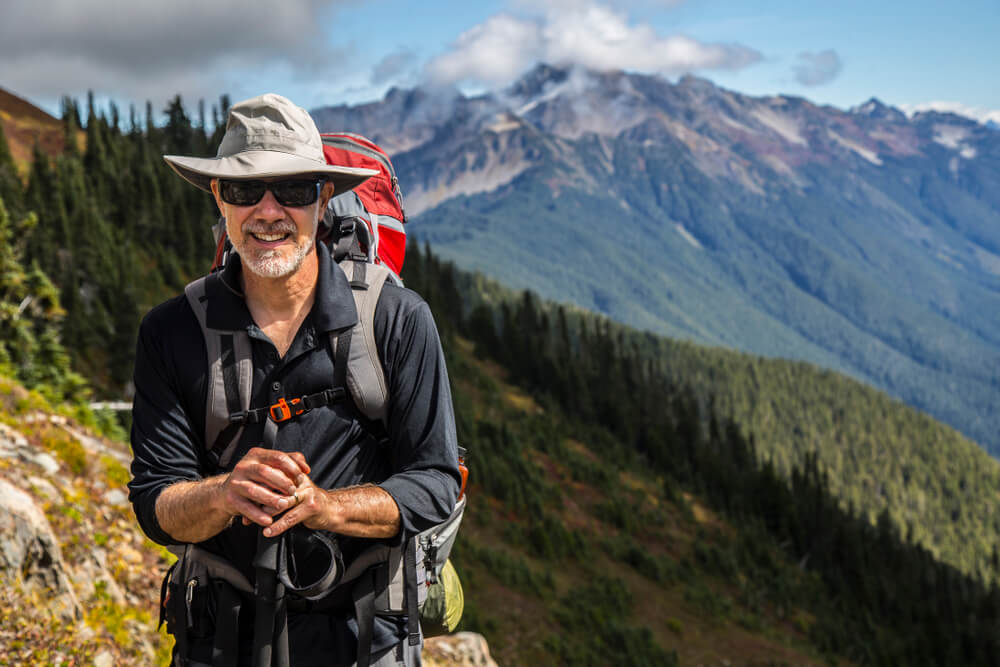 Hiker poses in front of mountain peaks range hiking
