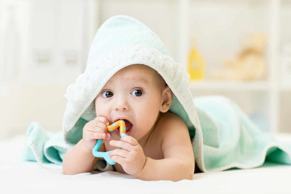 baby with teether in mouth under bathing towel