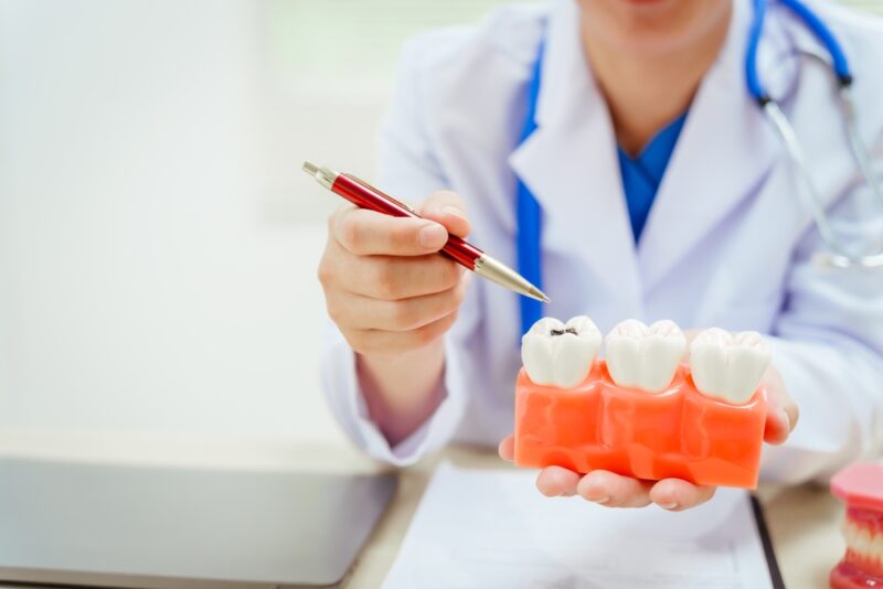 A bespectacled male doctor sits at a desk explaining about tooth decay