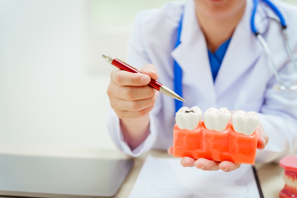 A bespectacled male doctor sits at a desk explaining about tooth decay