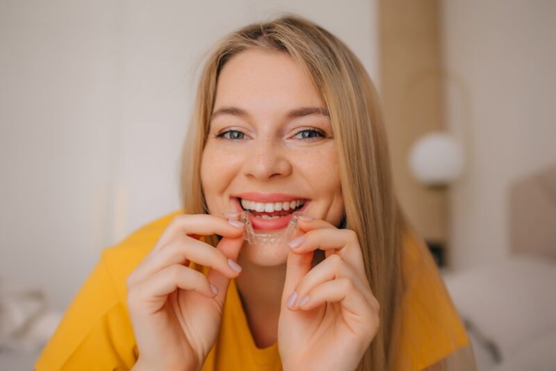 Young woman holding and using a clear aligner, promoting dental care and healthy oral practices