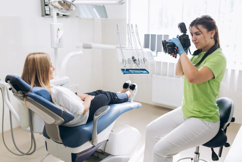 Dentist making shots of patients smile after treatment. Special camera with flash ring shadowless