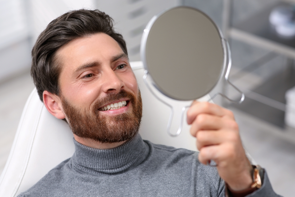 A man smiling in a mirror after receiving Preventative Care for his teeth