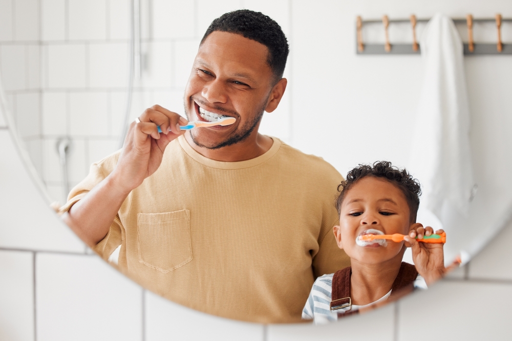 A child brushing their teeth with their parent after receiving Pediatric Dentistry 
