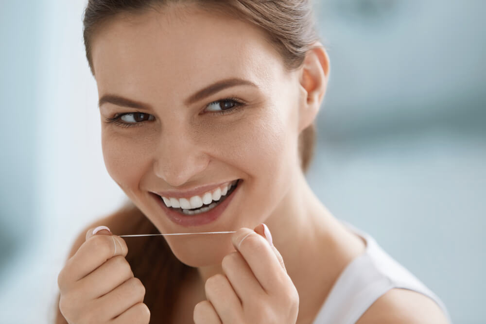 Smiling woman cleaning white teeth with floss