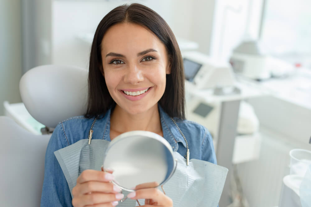 smiling woman sitting in dental chair holding mirror
