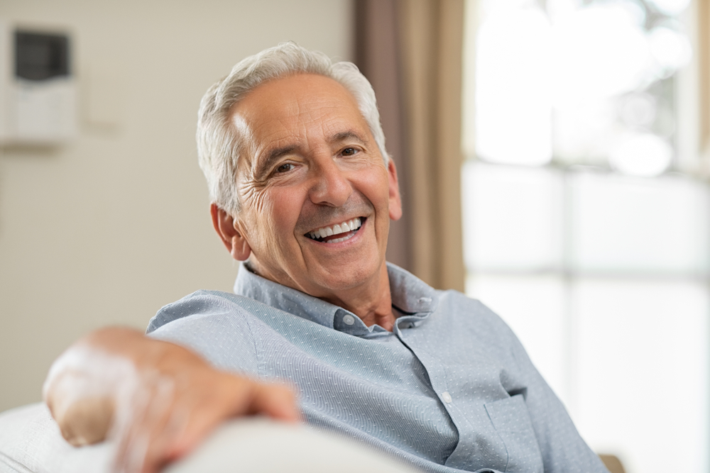 Portrait of happy senior man smiling at home. Old man relaxing on sofa and looking at camera.