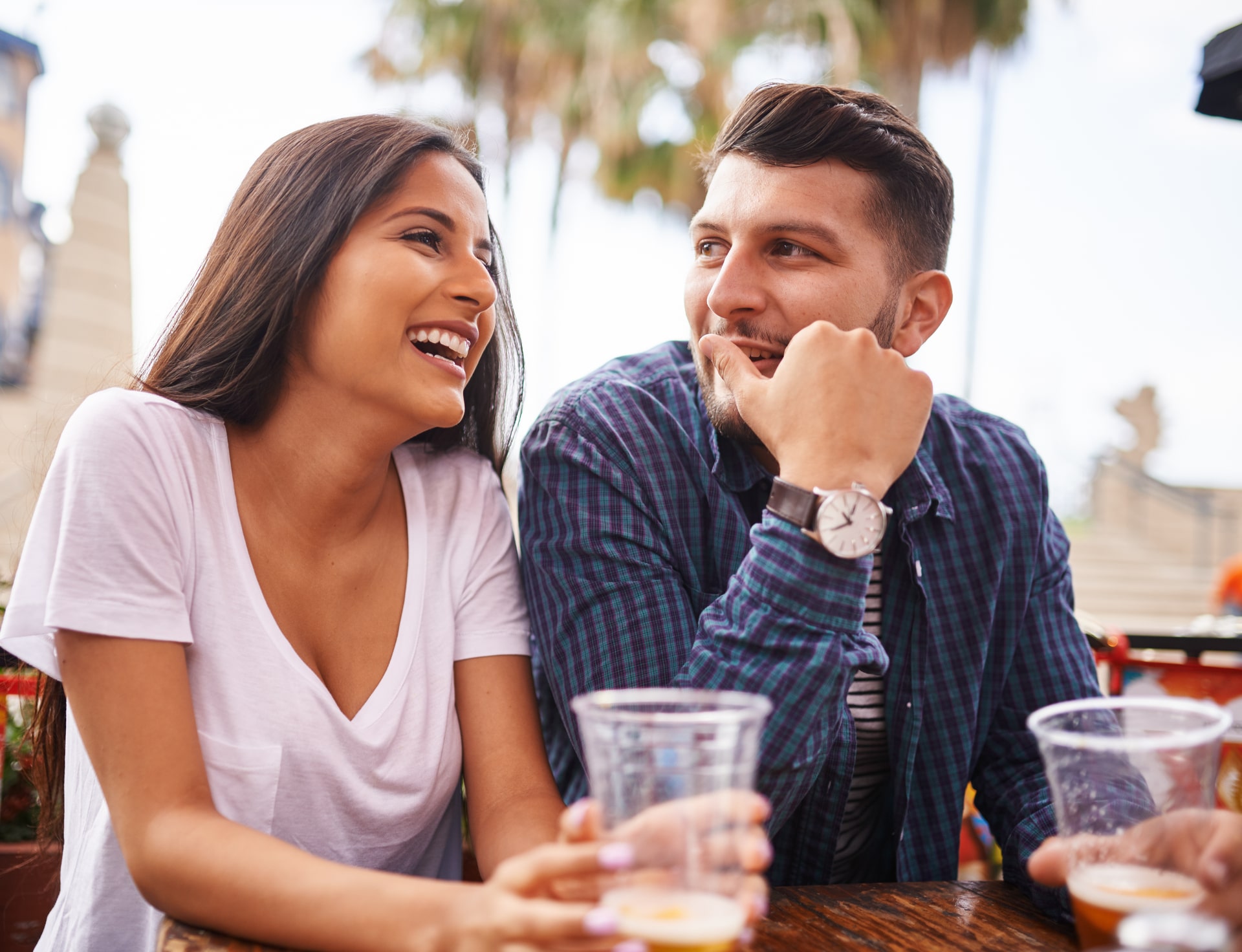 attractive hispanic couple drinking beer and having fun at outdoor restaurant